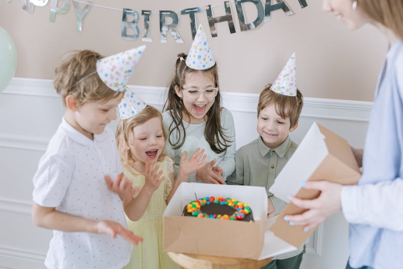 Kids in party hats clapping around a birthday cake